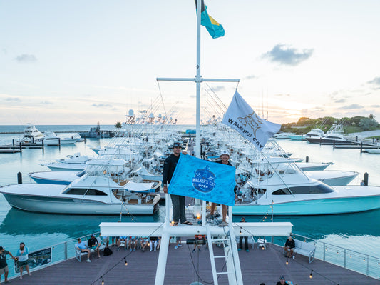 South Florida Sails AC team on the tower holding the SFC Walker's Cay Open pennant with the full tournament fleet behind them at sunset in Walker's Cay marina, May 2026.